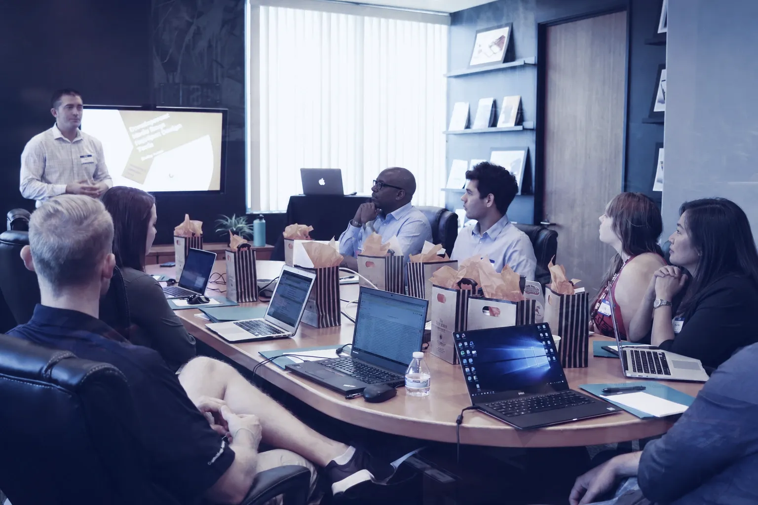 A team with laptops around a conference table, listening to a colleague present